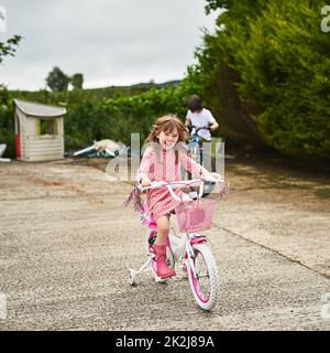 Bald Shell werden ohne Training Räder fahren. Porträt eines entzückenden kleinen Mädchens, das mit ihrem Bruder im Freien auf dem Fahrrad reitet. Stockfoto