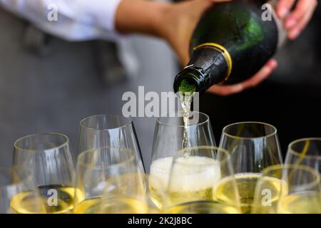 Nahaufnahme einer Champagnerflasche, die Champagner auf einer Sektflöte gegen eine verschwommene Person auf einer Party umschaufelt Stockfoto