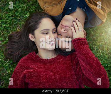 Mit dir neben mir ist das Leben komplett. High-Angle-Aufnahme eines glücklichen jungen Paares, das zusammen auf dem Gras liegt. Stockfoto