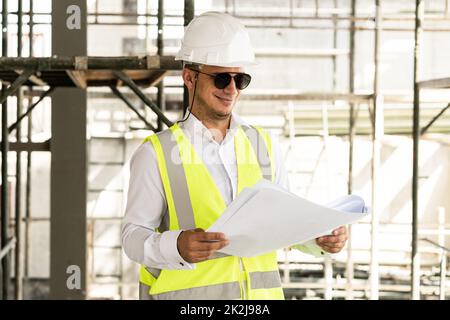 Mann Architekt trägt Sicherheitsweste mit einem Bauplan auf einer Baustelle Stockfoto