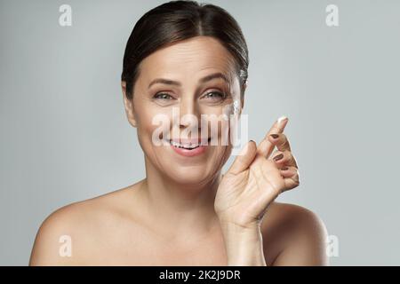 Frau mittleren Alters, die Anti-Aging-Creme auf ihr Gesicht auftragen Stockfoto