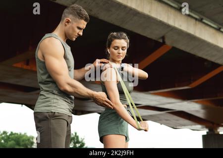 Frau während des Trainings mit einem persönlichen Fitnesstrainer mit Gummibändern im Freien Stockfoto