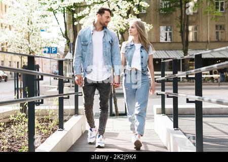 Liebevolles Paar in Jeansbekleidung, das während seines Dates auf einer Straße spaziert Stockfoto