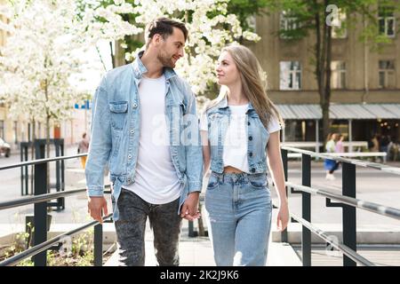 Liebevolles Paar in Jeansbekleidung, das während seines Dates auf einer Straße spaziert Stockfoto