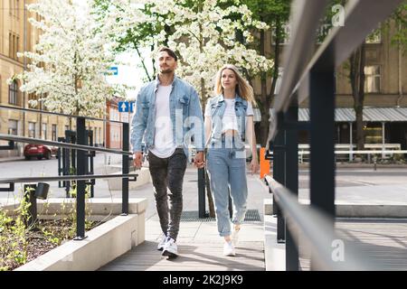 Liebevolles Paar in Jeansbekleidung, das während seines Dates auf einer Straße spaziert Stockfoto