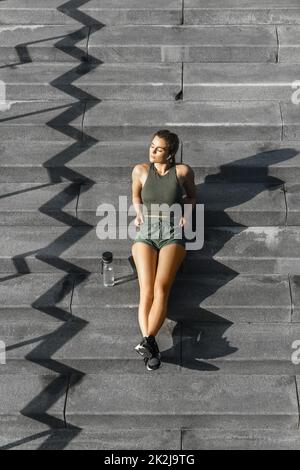 Sportliche Frau, die nach dem Fitness- oder Joggingtraining auf einer Treppe sitzt Stockfoto