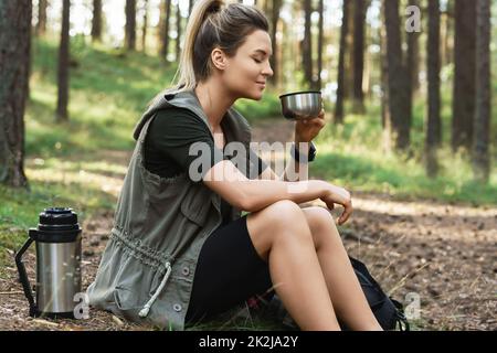 Wandern Sie während einer kleinen Pause mit einer Vakuumflasche, die heißen Kaffee oder Tee im grünen Wald trinkt Stockfoto