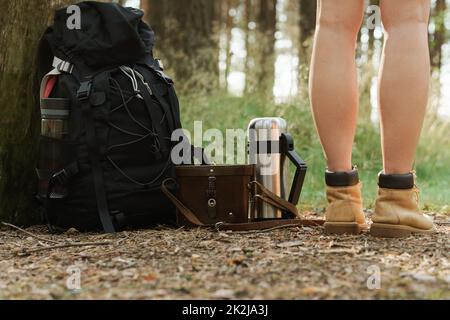 Weibliche Beine und Wanderrucksack auf dem Boden Stockfoto