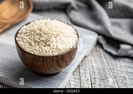 Ungekochter Carnaroli Risotto Reis in Schüssel auf Holztisch. Stockfoto