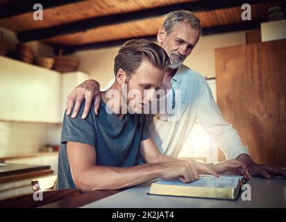 Sie ist eine Familie, die im Glauben gestärkt wurde. Aufnahme eines Vaters und eines Sohnes, die zu Hause gemeinsam Bibelstudien machen. Stockfoto