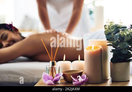 Zeit, die Dinge zu verlangsamen. Aufnahme der wichtigsten Spa-Anwendungen auf einem Tisch mit einer Frau, die im Hintergrund eine Massage bekommt. Stockfoto