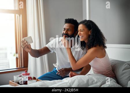 Beginnen Sie den Tag mit Essen, Liebe und Lachen. Ein junges, attraktives Paar, das zu Hause ein Selfie beim Frühstück im Bett gemacht hat, wurde in der Cropped-Aufnahme gedreht. Stockfoto