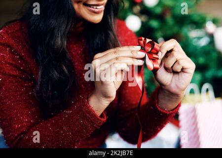 Es ist Weihnachten, gehen Sie hin und seien Sie ein bisschen extra. Aufnahme einer unkenntlichen Frau, die zu Hause ein Weihnachtsgeschenk verpackt. Stockfoto