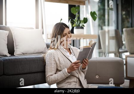 Lesen ist bei weitem das erfolgreichste Streben nach Glück. Eine kurze Aufnahme einer schönen jungen Frau, die ein Buch liest, während sie sich zu Hause entspannt. Stockfoto