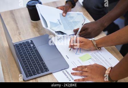 Durchsieben der Daten. Eine Aufnahme von zwei nicht erkennbaren Geschäftsleuten, die Papierkram durchmachen und in einem Büro einen Laptop verwenden. Stockfoto