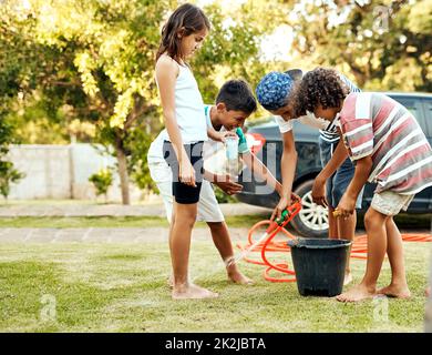 Scheuern Sie den ganzen Abrieb weg. Aufnahme einer Gruppe fröhlicher junger Kinder, die tagsüber draußen ihr Elternauto waschen. Stockfoto