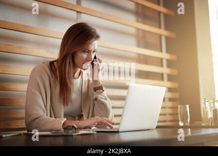 Schaffung von Geschäftsmöglichkeiten im Café. Aufnahme einer jungen Frau, die auf einem Mobiltelefon spricht, während sie in einem Café an ihrem Laptop arbeitet. Stockfoto