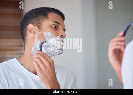 Es ist Zeit, alles abzurasieren. Aufnahme eines jungen Mannes, der sich in einem Badezimmer zu Hause den Bart rasiert. Stockfoto