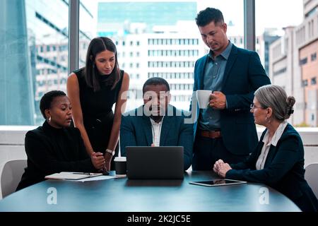 Ich brauche euch alle, um diese Präsentation zu sehen. Aufnahme eines Teams von Geschäftsleuten, die sich in einem Büro um einen Laptop versammelten. Stockfoto