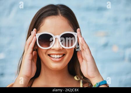 Shades on und bereit für den Sommer. Das verkürzte Porträt einer attraktiven jungen Frau, die ihre Sommertöne draußen vor einem blauen Hintergrund trägt. Stockfoto