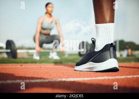 Sich der Fitness verschrieben. Nahaufnahme eines nicht erkennbaren männlichen Athleten, der draußen steht, während eine Frau mit Gewichten im Hintergrund trainiert. Stockfoto