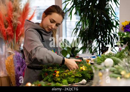 Minsk, Weißrussland - 20. Dez 2021: Floristin bei der Arbeit in einem Blumengeschäft macht einen Weihnachtskranz für das neue Jahr Stockfoto