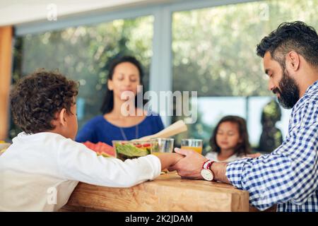 Gib uns heute unser tägliches Brot. Aufnahme einer Familie, die gemeinsam betet, bevor sie ein Essen am Tisch genießt. Stockfoto