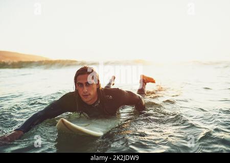 Beim Surfen geht es darum, den Rhythmus des Ozeans zu spüren. Porträt eines jungen Mannes, der auf einem Surfbrett im Meer paddelt. Stockfoto