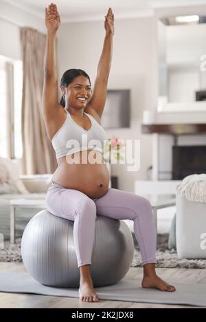 Stretching sicher hilft bei Schwangerschaftsschmerzen und Schmerzen. Aufnahme einer schönen jungen Schwangeren, die zu Hause trainiert. Stockfoto