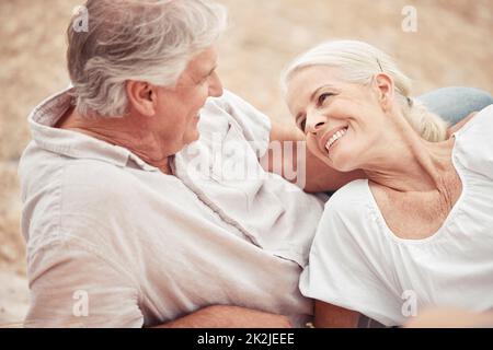Seniorenpaar, Strand und Urlaub mit einem Lächeln, Liebe und zusammen, während im Sommer gemeinsam auf dem Sand entspannen. Ältere Männer und Frauen genießen Romantik Stockfoto