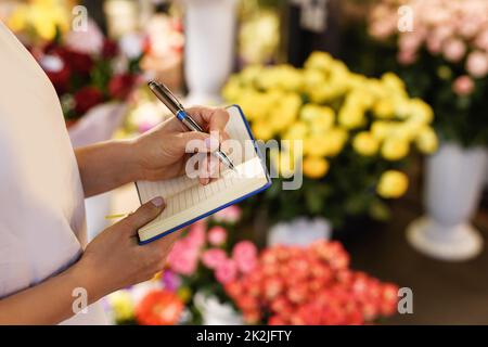 Frau Floristin macht Notizen in ihrem Notizbuch Stockfoto