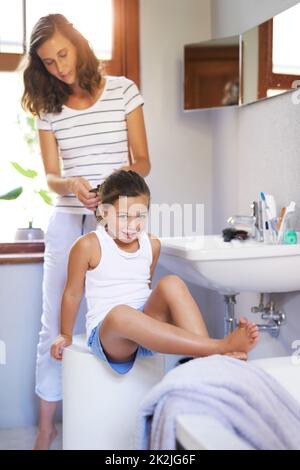 Mama gibt immer ihre Frisuren fit für eine Prinzessin. Aufnahme einer Mutter, die ihre kleinen Töchter zu Hause mit Haaren stylt. Stockfoto