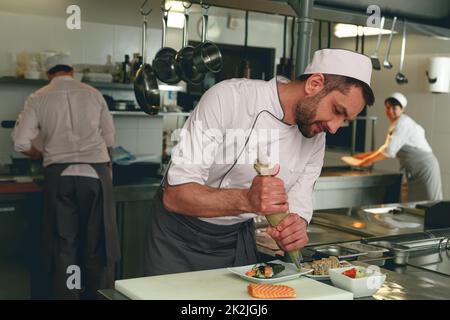 Professioneller Chefkoch in Uniformen, der Sushi in einer Küche des asiatischen Restaurants zubereitet Stockfoto