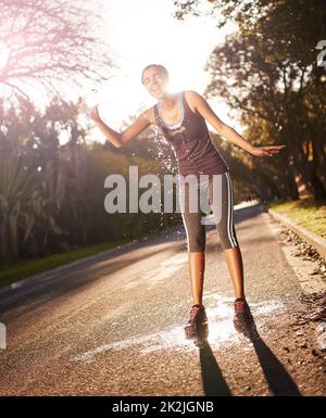 Das nach dem Training Gefühl ... Aufnahme einer jungen Frau, die nach einem intensiven Training kaltes Wasser über ihren Kopf gießt. Stockfoto