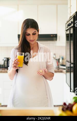 Etwas Vitamin C zu meinen Vitaminen. Aufnahme einer jungen Schwangeren, die zu Hause Medikamente mit Orangensaft einnehmen. Stockfoto