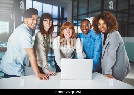 Moderne Technik gibt den Vorsprung auf. Ein Porträt einer Gruppe junger Geschäftsleute, die sich in ihrem Büro um einen Laptop drängten. Stockfoto
