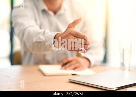 Willkommen in unserem Unternehmen. Aufnahme eines nicht identifizierbaren Geschäftsmannes, der seine Hand zum Händeschütteln über einen Tisch im Büro streckte. Stockfoto