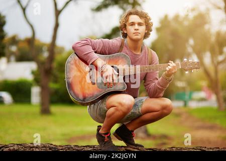 Kann ich Euch eine kleine Melodie spielen? Porträt eines jungen Mannes, der draußen Gitarre spielt. Stockfoto