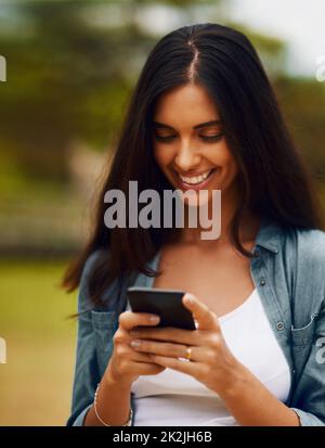 Was sind alle anderen bis zu diesem Wochenende. Aufnahme einer attraktiven jungen Frau, die in einem Park ein Mobiltelefon benutzt. Stockfoto