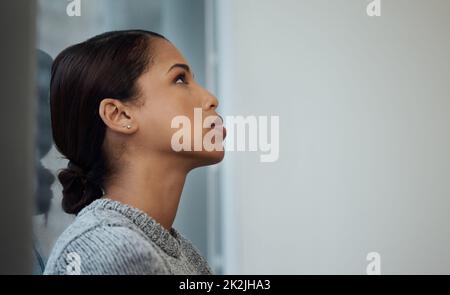 Ich fühle mich in letzter Zeit so blau. Aufnahme einer jungen Geschäftsfrau, die eine Pause einnahm und sich an ein Fenster lehnte. Stockfoto