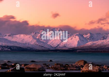Das türkisfarbene Wasser des Lake Tekapo ist kurz nach Sonnenuntergang zu sehen. In der Ferne befindet sich das Mount Cook Gebirge in der Südalp von Neuseeland. Stockfoto
