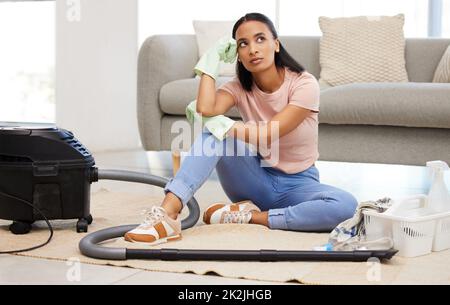 Muss ich all diese Reinigungsarbeiten machen? Aufnahme einer jungen Frau, die auf dem Boden sitzt und zu Hause nachdenklich aussieht. Stockfoto