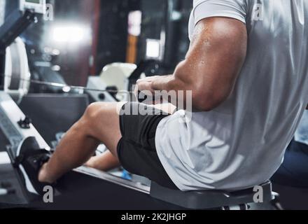 Arbeitet seinen ganzen Körper. Zugeschnittenes Bild eines nicht erkennbaren männlichen Athleten, der im Fitnessstudio auf einem Rudergerät trainieren soll. Stockfoto