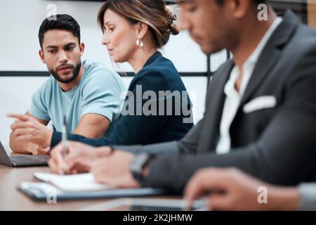 Austausch von Ideen und Informationen. Eine Aufnahme von zwei jungen Geschäftsleuten, die während eines Gesprächs mit ihren Kollegen im Sitzungssaal sprechen. Stockfoto