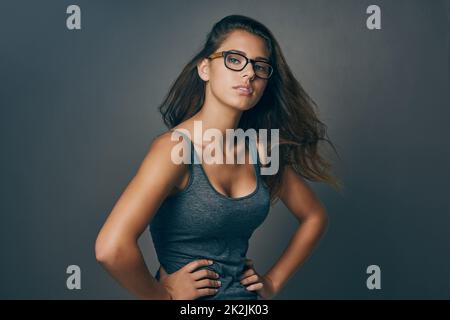 Kanalisieren Sie Ihren inneren Nerd. Studio-Aufnahme einer attraktiven jungen Frau, die vor grauem Hintergrund posiert. Stockfoto