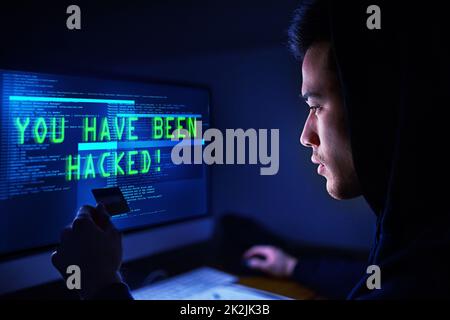 Ihr Geld gehört mir jetzt. Aufnahme eines verdunkelten Computerhackers, der einen Computer im Dunkeln benutzt. Stockfoto