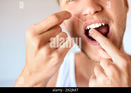 Bringen Sie Ihre Zahnhygiene in die Höhe. Nahaufnahme eines jungen Mannes, der zu Hause seine Zähne mit Zahnseide verputzt hat. Stockfoto