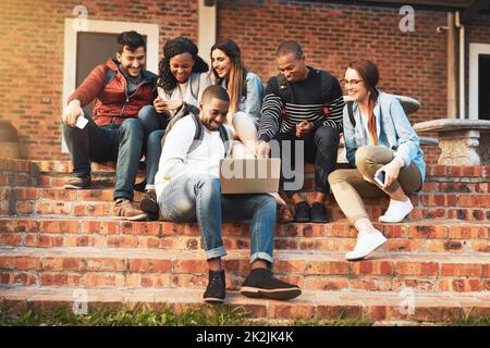 Sich mit Gleichgesinnten zu verbinden. Aufnahme einer Gruppe von Studenten, die zusammen auf dem Campus einen Laptop benutzen. Stockfoto