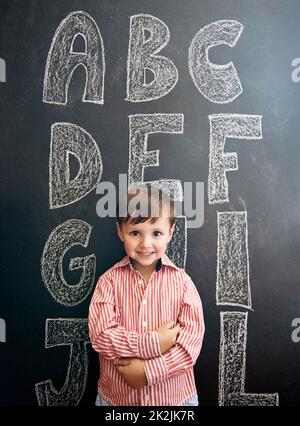 Meine ABCs wurden gemein. Porträt eines entzückenden kleinen Jungen, der vor einer Tafel mit Buchstaben auf der Tafel steht. Stockfoto