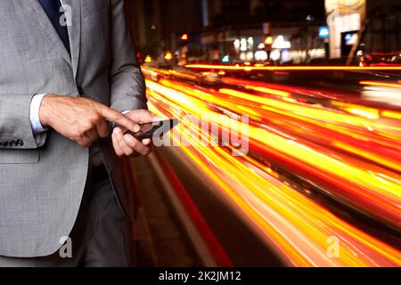 Mit dieser App bekomme ich in kürzester Zeit ein Taxi. Eine ausgeschnittene Aufnahme eines Geschäftsmannes, der an einer belebten Straße steht und eine SMS schreibt. Stockfoto